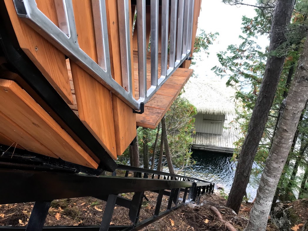 Looking down the track to the floating dock before the lower station was built. We trimmed the gate so the car can travel up and down even when the gate is fully open, without harming the gate. The lake level rises and falls by nearly six feet, so Stu had us set the car just above the nominal high-water mark. His crew then added a new lower access platform connecting the lift, the staircase, and the floating dock—brilliant work. The track's visual and environmental footprint is far lower than a staircase, with the added benefit that everyone can travel between the cottage and the water; no one is left stuck in the cottage.